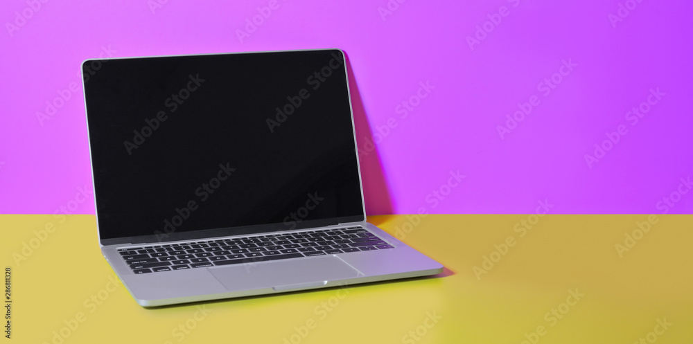 Open laptop computer on yellow desk and pink wall background Open laptop computer on yellow desk and pink wall background