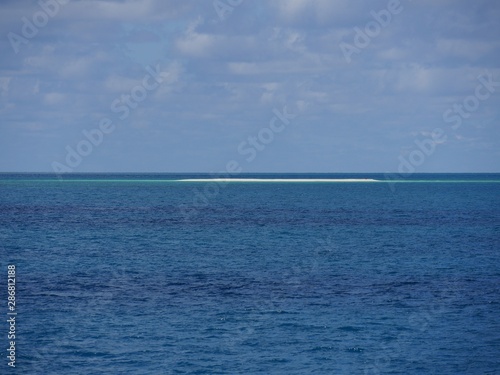 Wide shot of the ocean with a sliver of a white sand bar in the distance