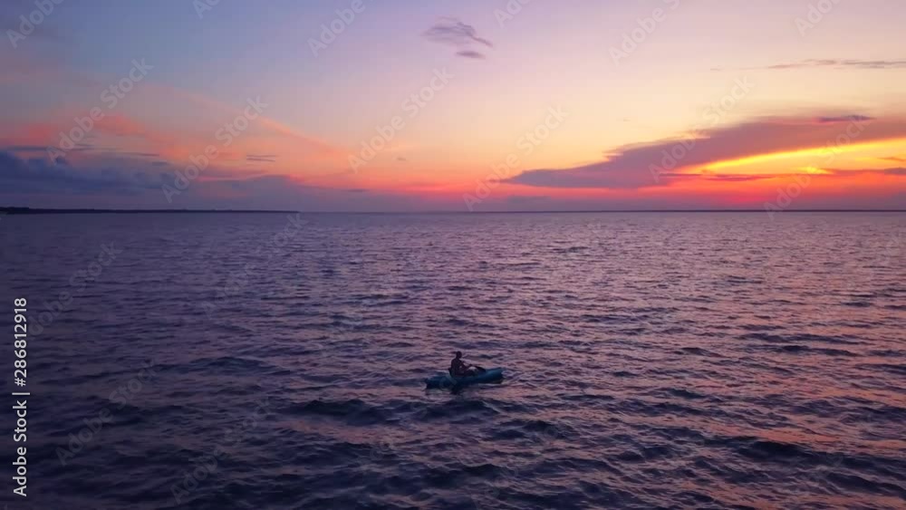 A dramatic drone shot of a lone kayaker slowly driffting into a colorful sunset A dramatic drone shot of a lone kayaker slowly driffting into a colorful sunset
