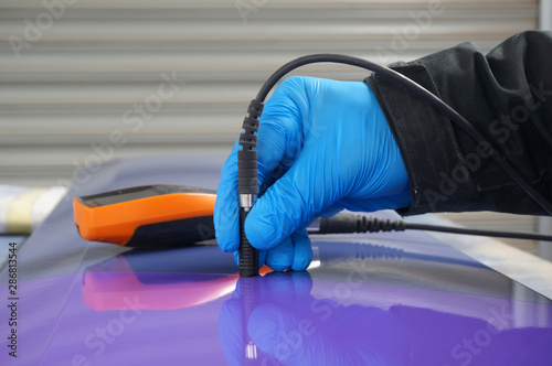 Photography Person using probe, with digital tester, to measure the paint thickness microns on a painted metal panel