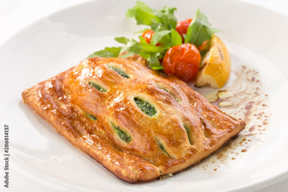 Puff pastry bun with spinach and tomato and lemon on the side isolated on white background Puff pastry bun with spinach and tomato and lemon on the side isolated on white background