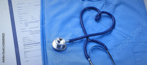 Fényképezés A medical stethoscope is intertwined in the shape of a heart and lies on a medical history and a blue uniform