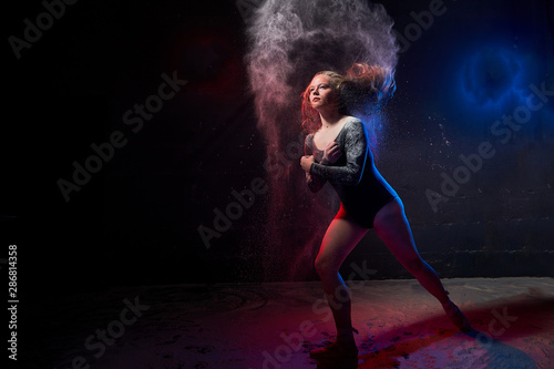 Young teen girl in a dark room during a photoshoot with flour with a colored light and a black background
