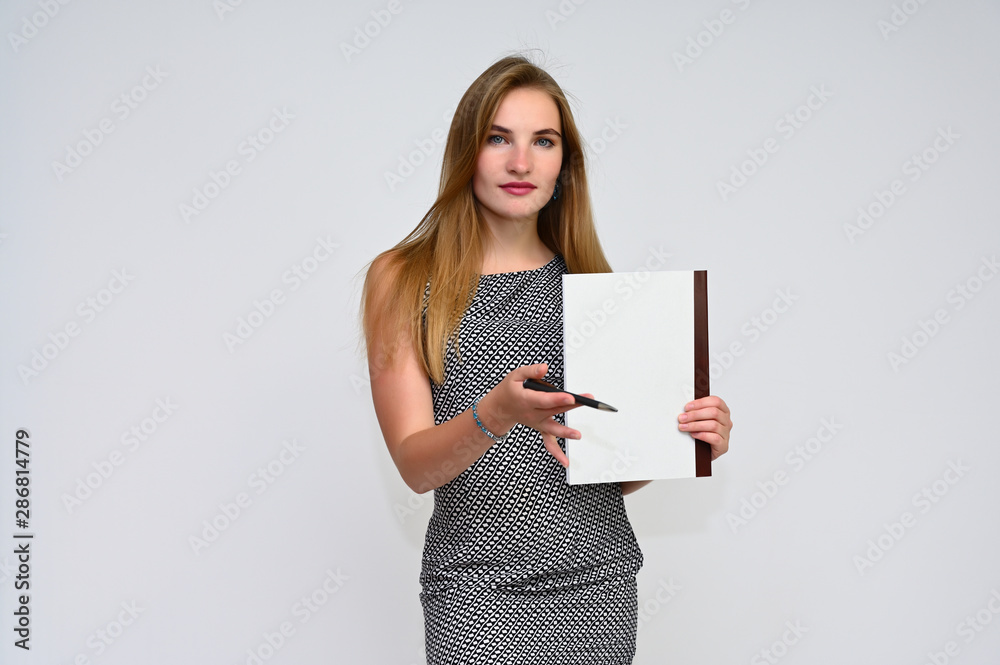 Portrait of a pretty brunette manager girl with long flying hair in a gray dress on a white background with a folder in her hands. Smiling, showing emotions. Portrait of a pretty brunette manager girl with long flying hair in a gray dress on a white background with a folder in her hands. Smiling, showing emotions.