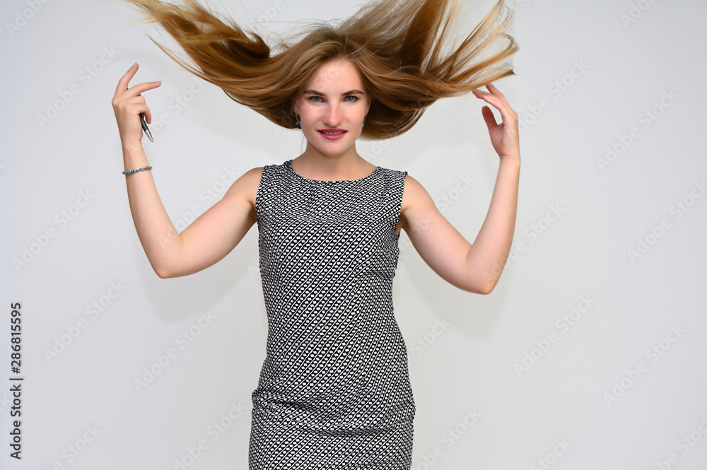 Portrait of a pretty brunette manager girl with long flying hair in a gray dress on a white background with a pen in her hands. Smiling, showing emotions. Portrait of a pretty brunette manager girl with long flying hair in a gray dress on a white background with a pen in her hands. Smiling, showing emotions.