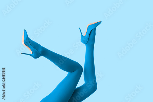 Legs of beautiful young woman in tights and high-heeled shoes on color background photo