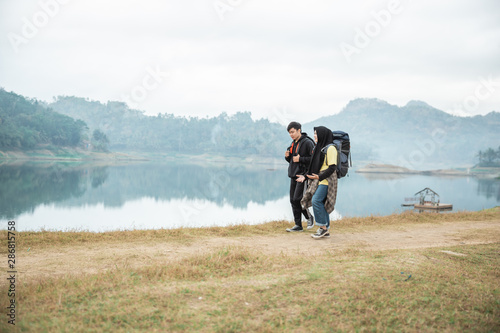 couple hikers with backpacks enjoying lake view, walking side the lake