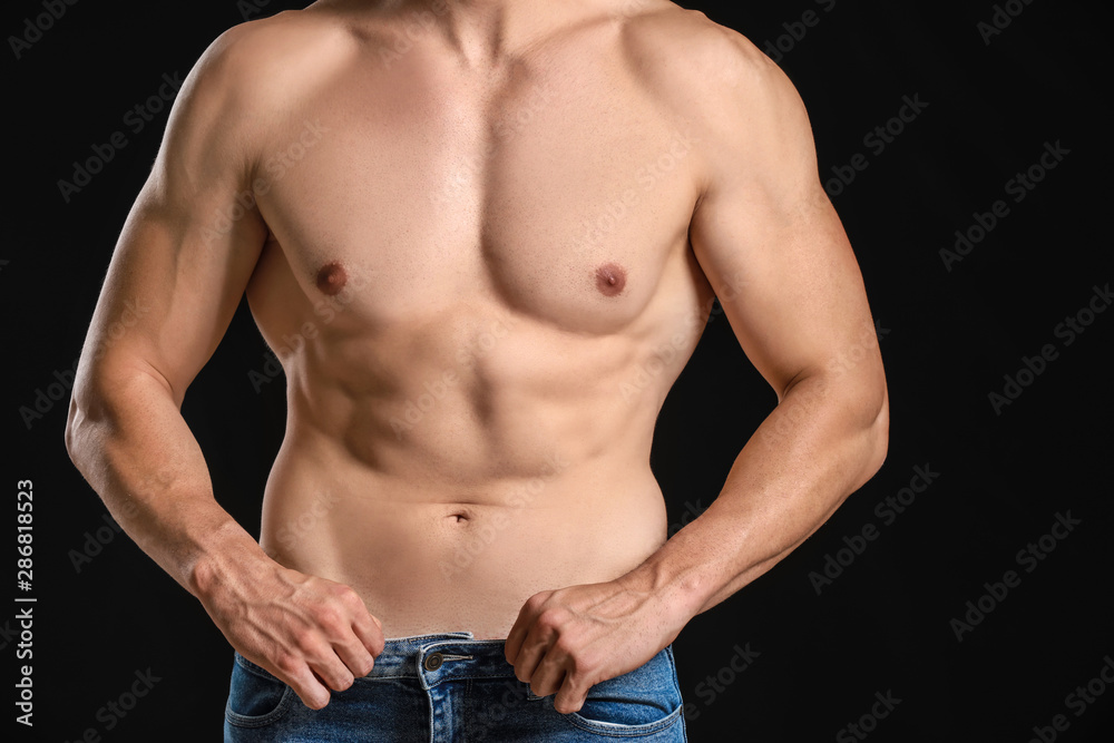 Handsome muscular man in loose jeans on dark background. Weight loss concept