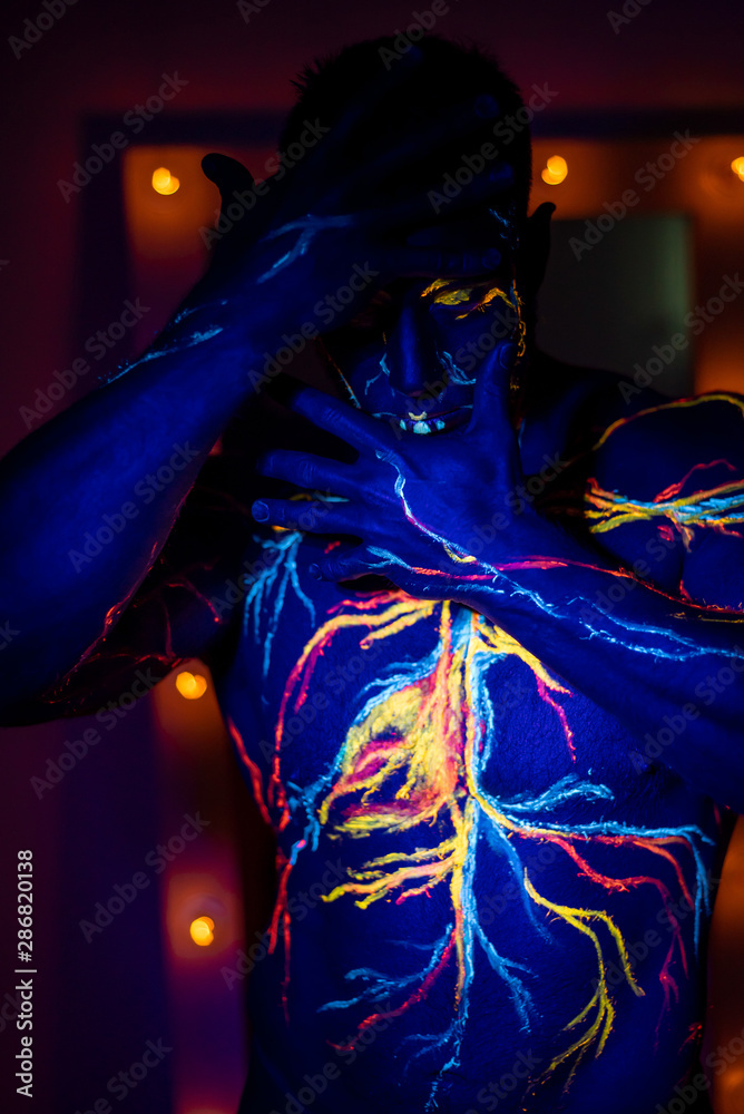 UV patterns body art of the circulatory system on a man's body. On the torso of a muscular athlete, veins and arteries are drawn with fluorescent dyes. Bodybuilder standing by the mirror with lamps.