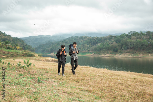 Two asian travelers standing near lake at sunny day