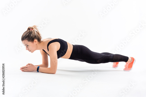 Young sporty blond woman in a black sportswear holding plank position exercising isolated over white background.
