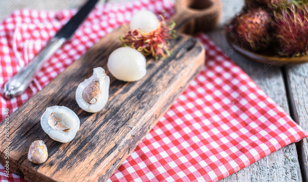Mix of whole and peeled rambutan on wooden cutting board and table. Rambutan is an exotic fruits from tropical countries. Mix of whole and peeled rambutan on wooden cutting board and table. Rambutan is an exotic fruits from tropical countries.