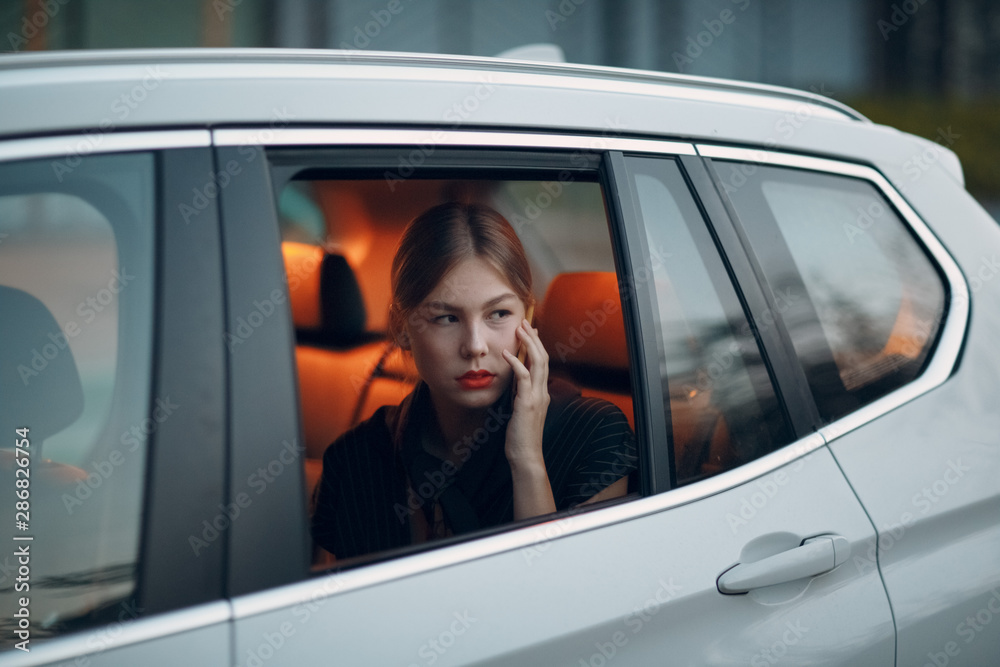 Young woman sitting in back seat of car vehicle with mobile phone. Taxi concept.