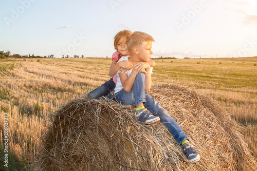 Obraz na plátně happy children sitting on haystack at sunset