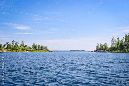 The surface of the lake is covered with ripples and waves against a rocky coast. Summer landscape in sunny weather.