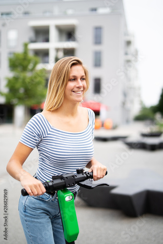 Sympathisch lachende junge Frau ist mit einem E-Scooter unterwegs 