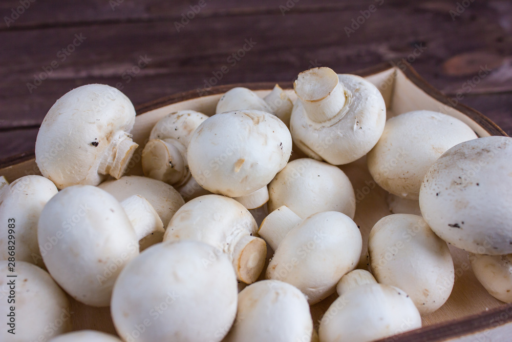 Champignon mushrooms in a wooden tray on a dark background Champignon mushrooms in a wooden tray on a dark background