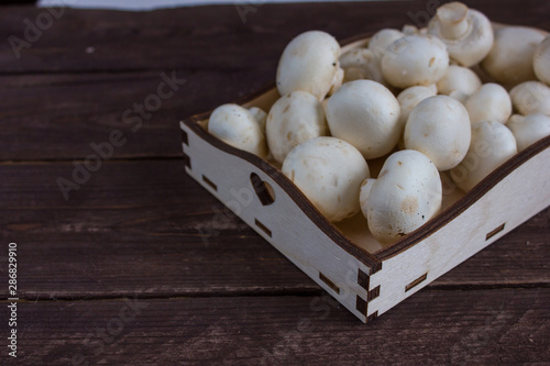 Champignon mushrooms in a wooden tray on a dark background