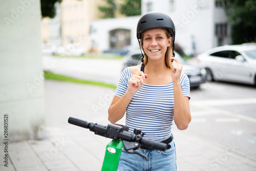 Konstfotografi Junge Frau zieht einen Helm an um mit einem E-Scooter zu fahren
