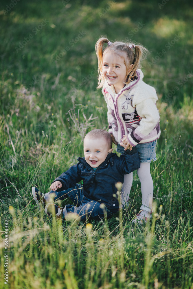 Little sister and brother posing in a green park.