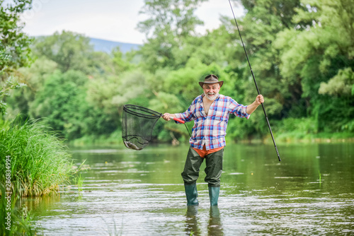 F for Fishing. hobby and sport activity. pothunter. fisherman with fishing rod. mature man fly fishing. man catching fish. retired bearded fisher. Trout bait. summer weekend. Big game fishing