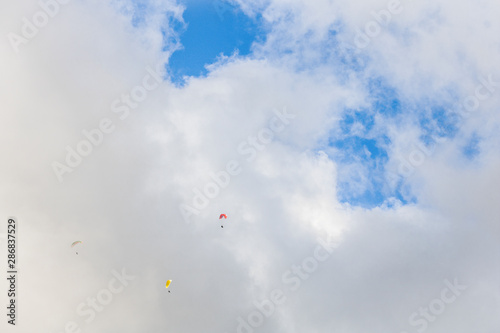 Paragliders floating through clouds and blue sky over Camps Bay, Cape Town.
