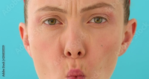 Woman posing at blank studio wall, frowning eyebrows, her look and grimace expressing anger, annoyance and irritation on blue background