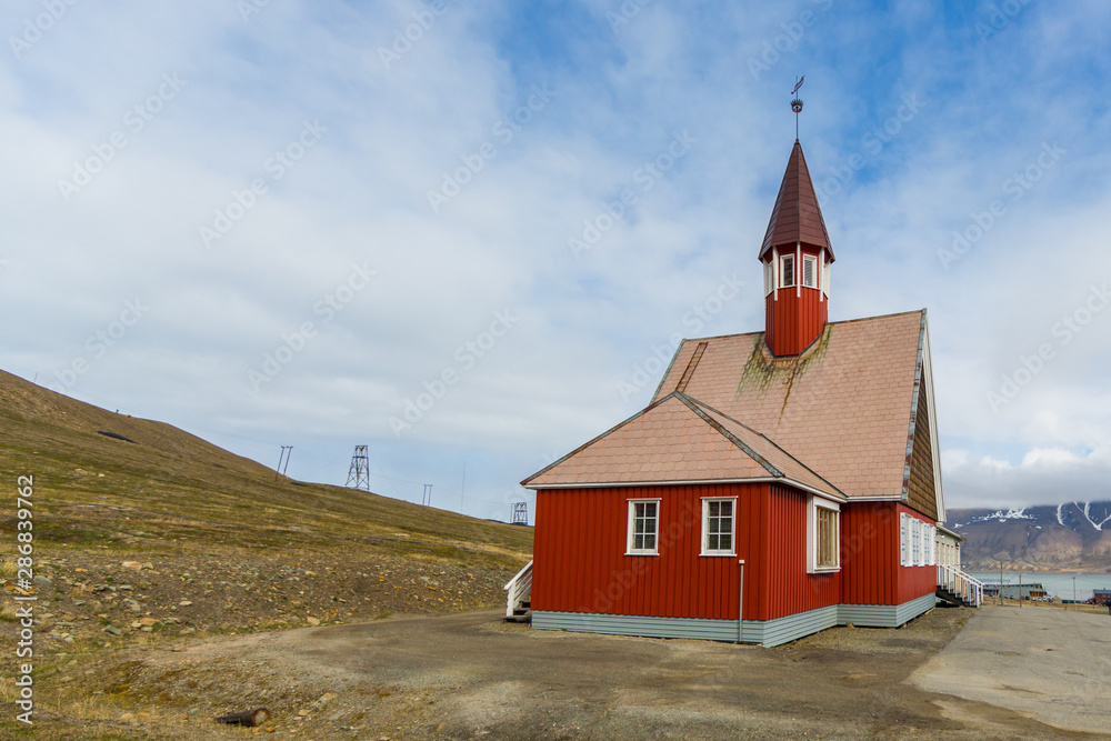 red Svalbard church in Longyearbyen, cloudy blue sky, sunlight