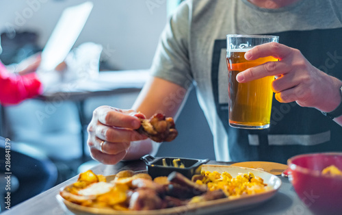 man hand with glass of cold beer and plate with snacks on wooden table background on bar or pub