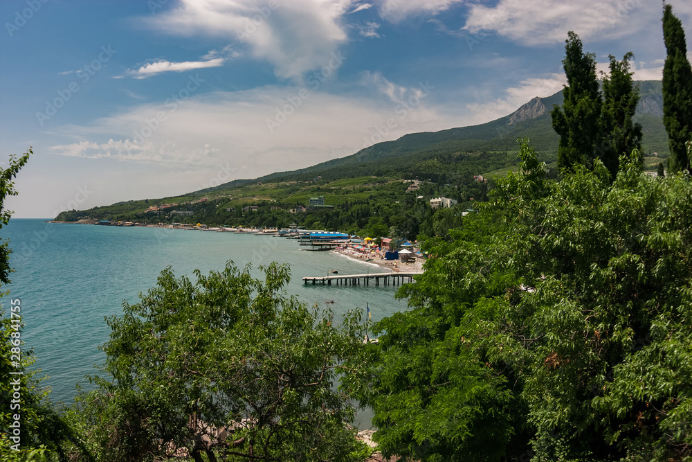 View to the city beach with umbrellas, sunbeds and people relaxing in cloudy day with mountains on the background. Black Sea.