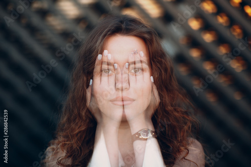 Portrait of shy young positive woman with hands on her face