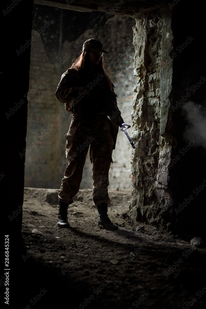Silhouette of warrior girl with weapon in full ammunition in doorway. Conceptual military photo