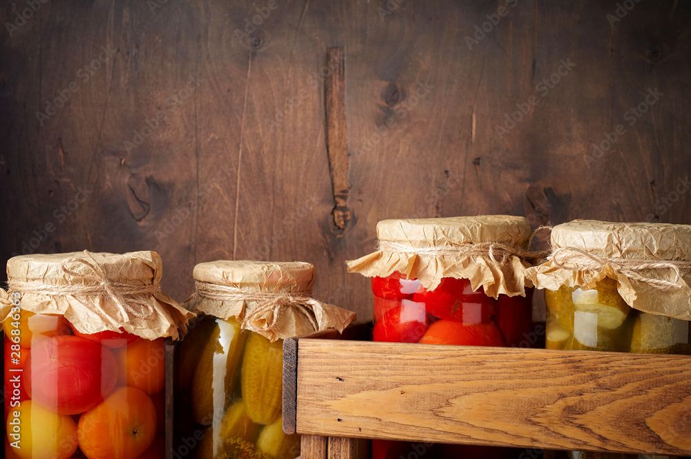 Homemade pickled tomato and cucumber in glass jars in wooden rustic box