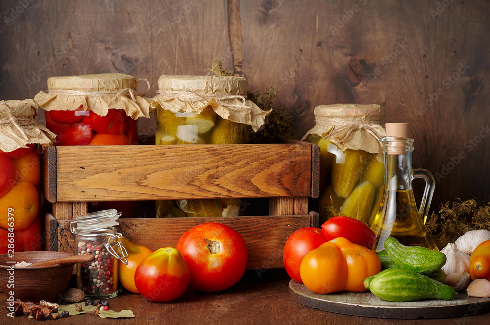 Homemade pickled tomato and cucumber in glass jars on an wooden rustic background