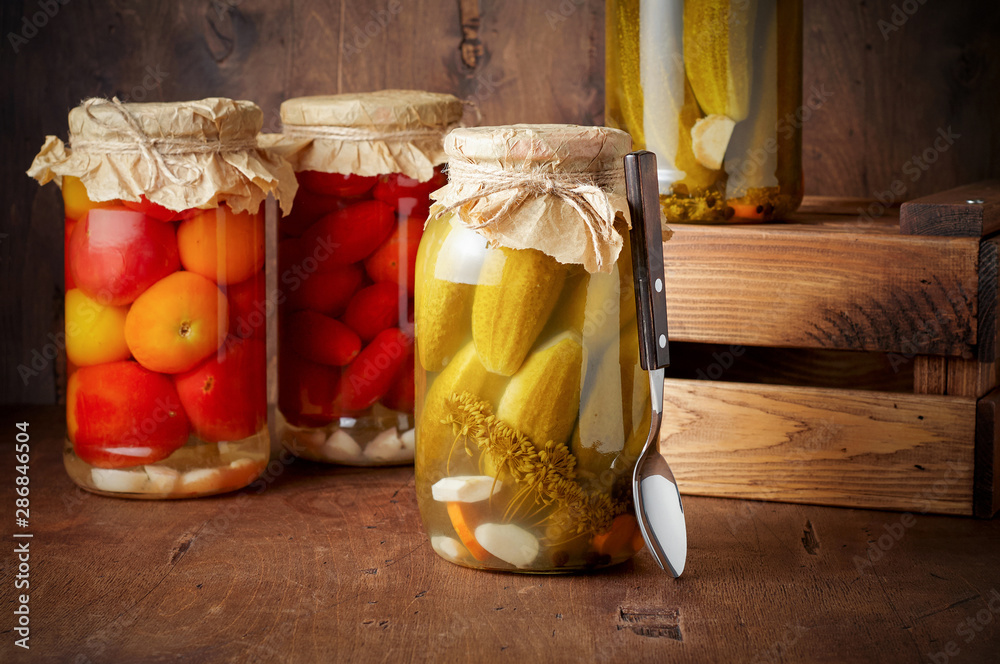 Homemade pickled tomato and cucumber in glass jars in wooden rustic box