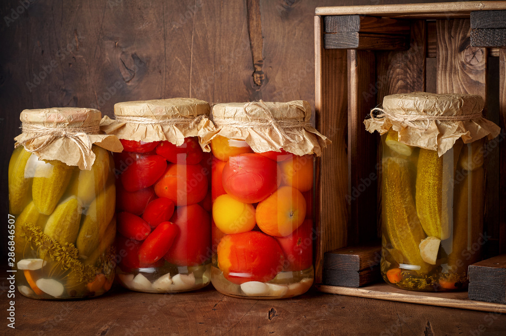 Homemade pickled tomato and cucumber in glass jars in wooden rustic box