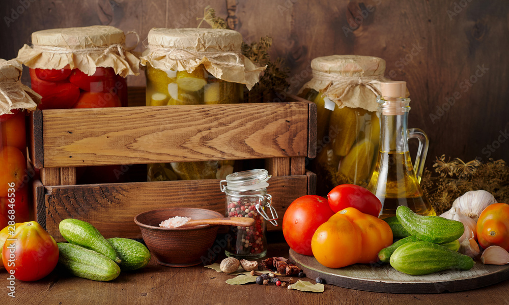 Homemade pickled tomato and cucumber in glass jars on an wooden rustic background