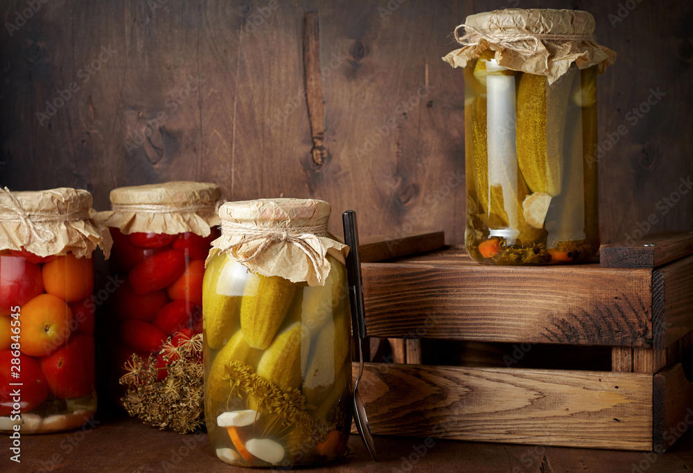 Homemade pickled tomato and cucumber in glass jars in wooden rustic box