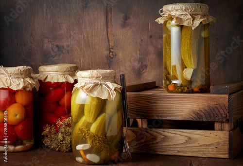 Homemade pickled tomato and cucumber in glass jars in wooden rustic box
