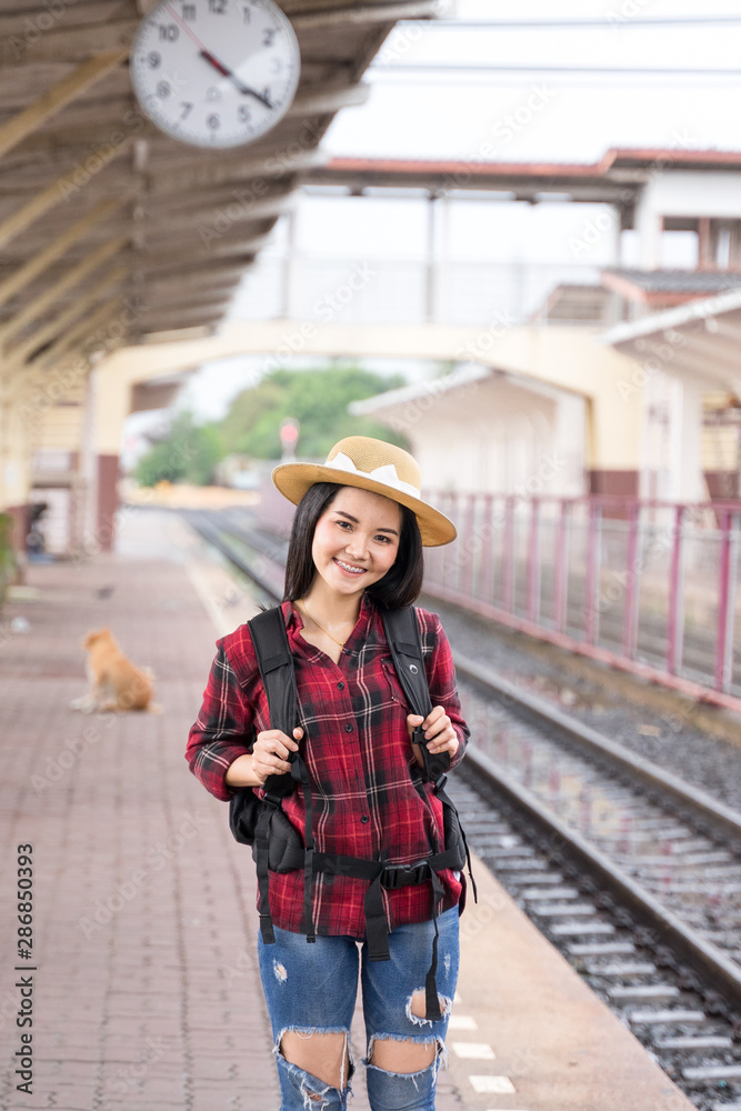 Young beautiful female travel photographer enjoys taking photo during her trip at railway station. Asian woman travel with camera having fun making pictures while waiting for train.