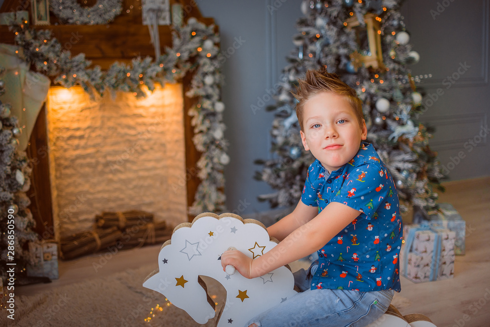 Boy rides a toy rocking horse, Christmas concept, fireplace and a toy tree in the background