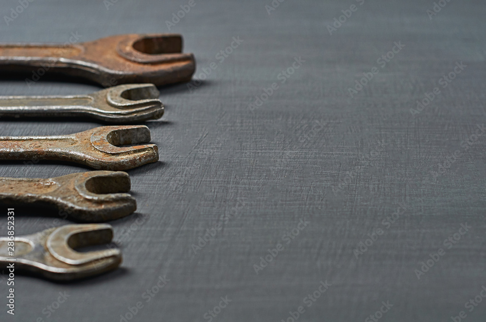 Row of old rusty and messy wrenches for nuts lies on dark concrete. Space for text Row of old rusty and messy wrenches for nuts lies on dark concrete. Space for text