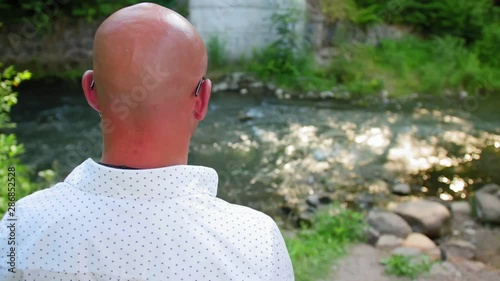 Rear view of a bald man looking at a river flowing under a bridge. Close up shot.