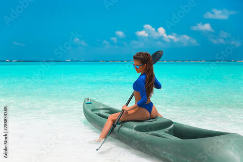 Sexy brunette paddling a kayak. Fashion Woman in blue bikini exploring calm tropical bay. Maldives island. Sporty activity. Summer water sport, adventure outdoors. © Victoria Andreas