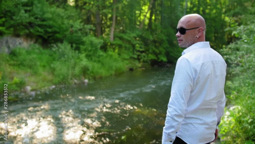 Side view of a bald man looking at the current river, under the bridge. Medium shot. Side view of a bald man looking at the current river, under the bridge. Medium shot.
