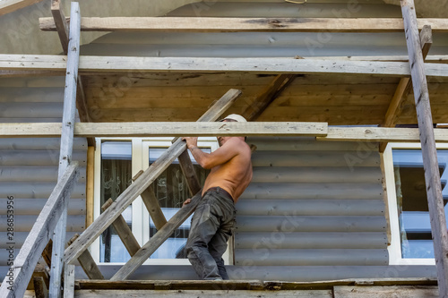 Male builder pulls a ladder on construction site of wooden house