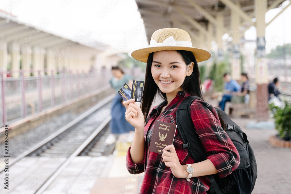 Young beautiful female travel photographer enjoys taking photo during her trip at railway station. Asian woman travel with camera having fun making pictures while waiting for train.