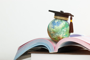 Study abroad education in Global ideas: Graduated cap on top global model on open textbook in library. Concept of studying international educational,reading book bring success degree in life
