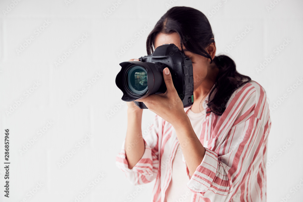 Female Photographer With Camera On Photo Shoot Against White Studio Backdrop Female Photographer With Camera On Photo Shoot Against White Studio Backdrop