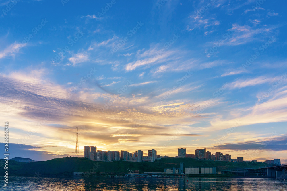 Naklejka premium Evening city of Krasnoyarsk on the banks of the Yenisei river at sunset. Beautiful view. Buildings of the new neighborhood. Beautiful sky.